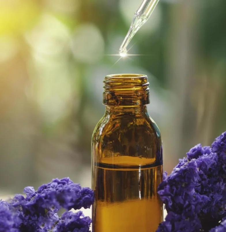 A dropper over an amber essence bottle with purple flowers